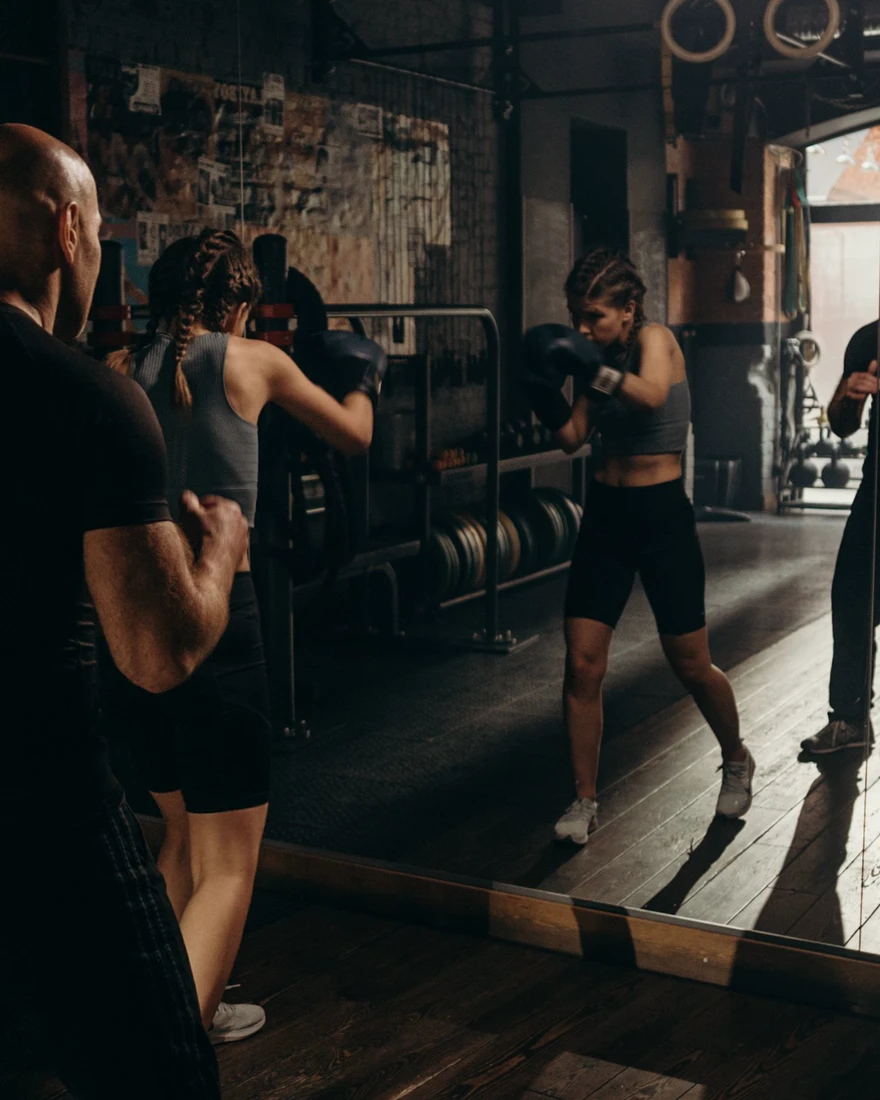 A boxer training with her coach in front of a gym mirror